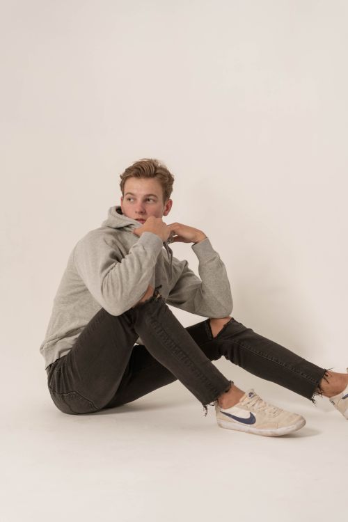 Free Young man in casual attire sitting on the floor in a studio setting, portraying a relaxed and thoughtful pose. Stock Photo