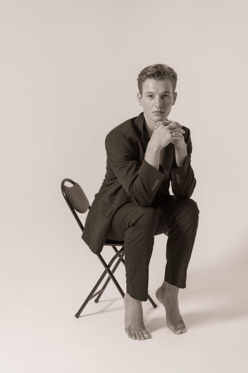 Free A black and white portrait of a man barefoot in a suit sitting in a studio. Stock Photo