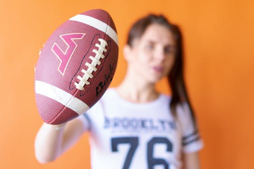 A Woman in White Crew Neck Shirt Holding a Brown Football
