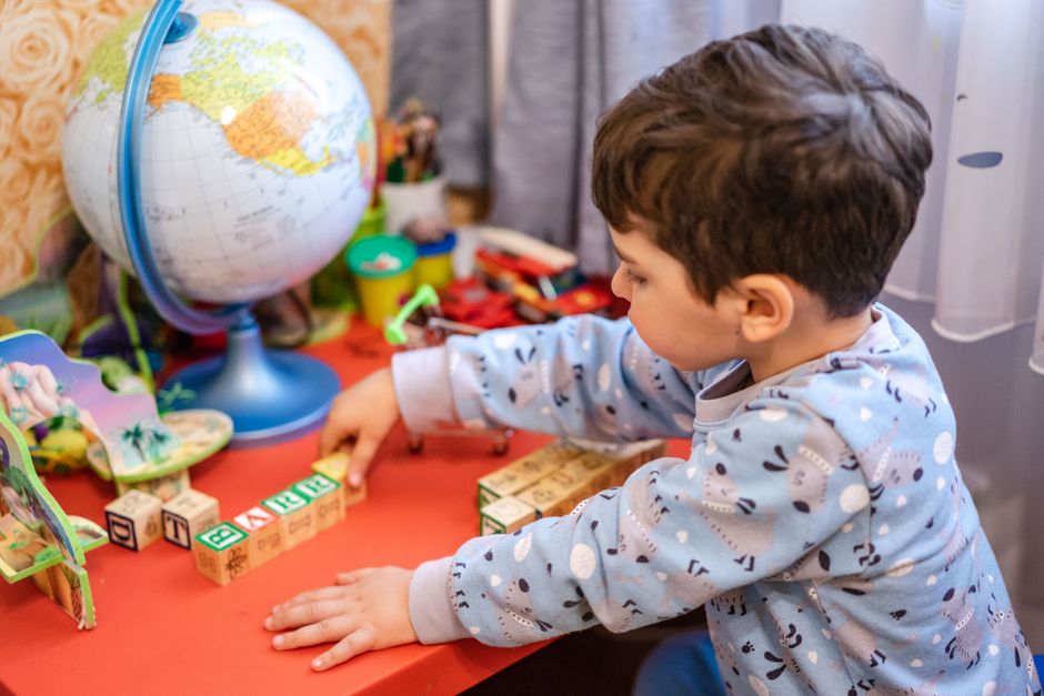 Photo by Atlantic Ambience on Pexels Ein kleiner Junge beschäftigt sich drinnen mit Alphabetblöcken und einem Globus und lernt spielerisch. - Foto von Atlantic Ambience auf Pexels