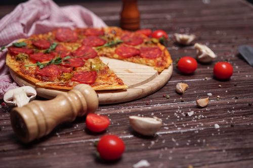 Free Close-up of pepperoni pizza on a wooden board with cherry tomatoes and garlic cloves on a rustic table. Stock Photo