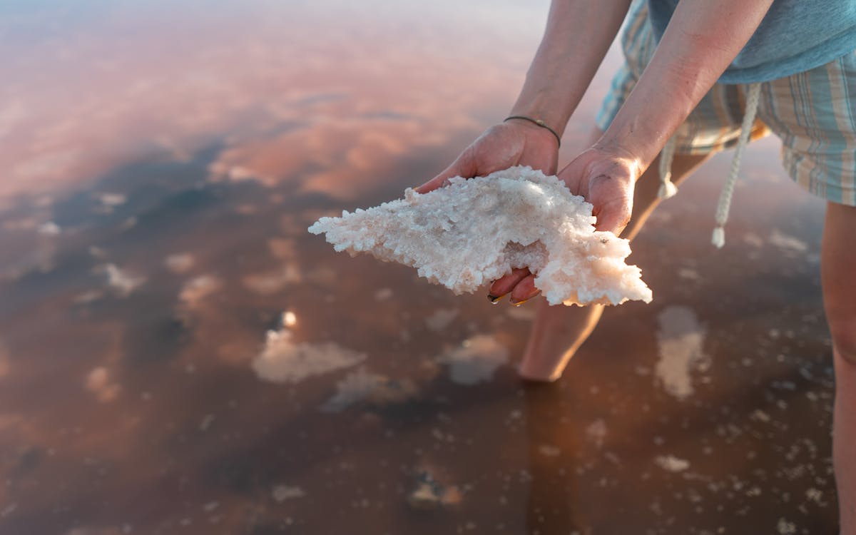 Close-up of hands holding salt crystals from a shallow saline lake at sunset.