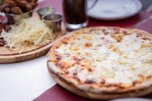 Close-up of a freshly baked cheese pizza with toppings and accompaniments on a wooden platter.