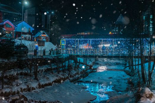 A frosty winter night scene with illuminated bridge and snow-covered landscape.