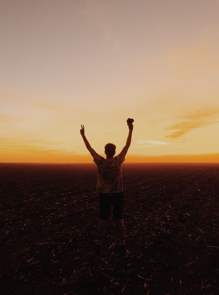 Silhouette Of Man With Hands Up In Field On Sunset