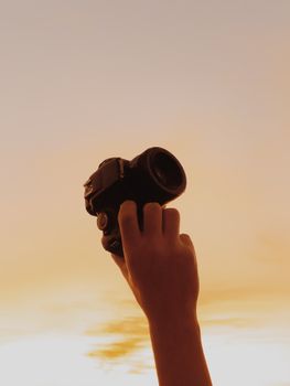 Silhouette of a hand holding a camera against a warm golden sky at sunset.