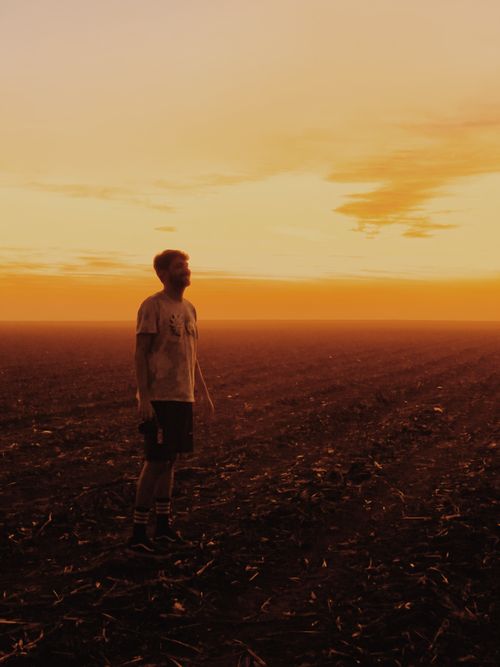 Free A man stands alone in an expansive field during a golden sunset, capturing serenity and solitude. Stock Photo