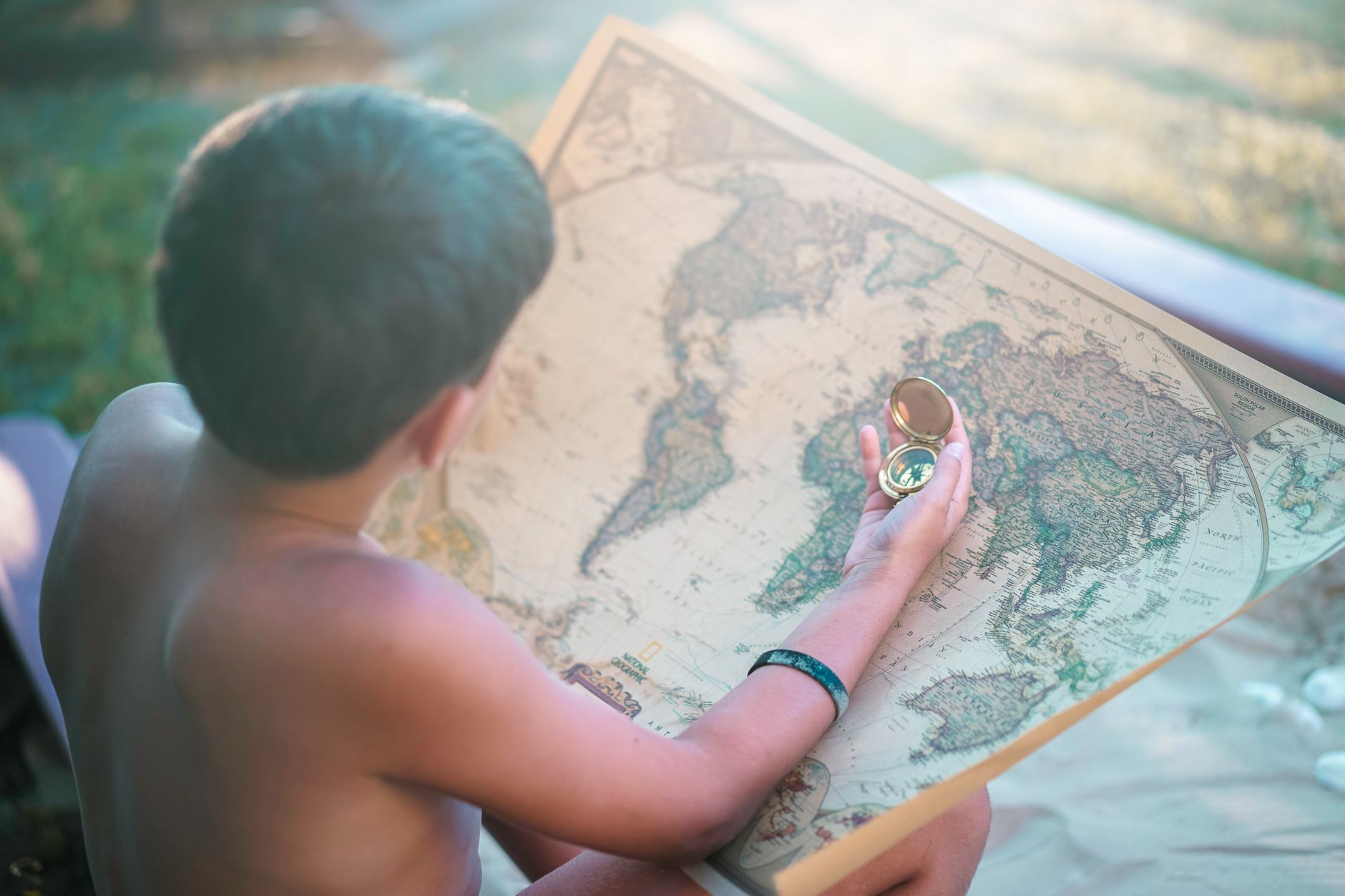 A child examines a world map with a compass in hand, capturing the essence of exploration and curiosity.