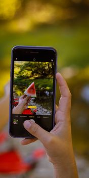 A hand holds a smartphone capturing a juicy watermelon slice in vibrant outdoor summer setting.