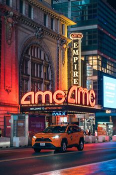 A colorful night scene of AMC theater in New York City with a taxi passing by.