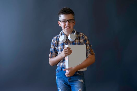 Smiling boy wearing headphones and glasses, holding a book against a plain dark background.