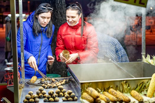 Two women preparing grilled corn and chestnuts at a night market stall.