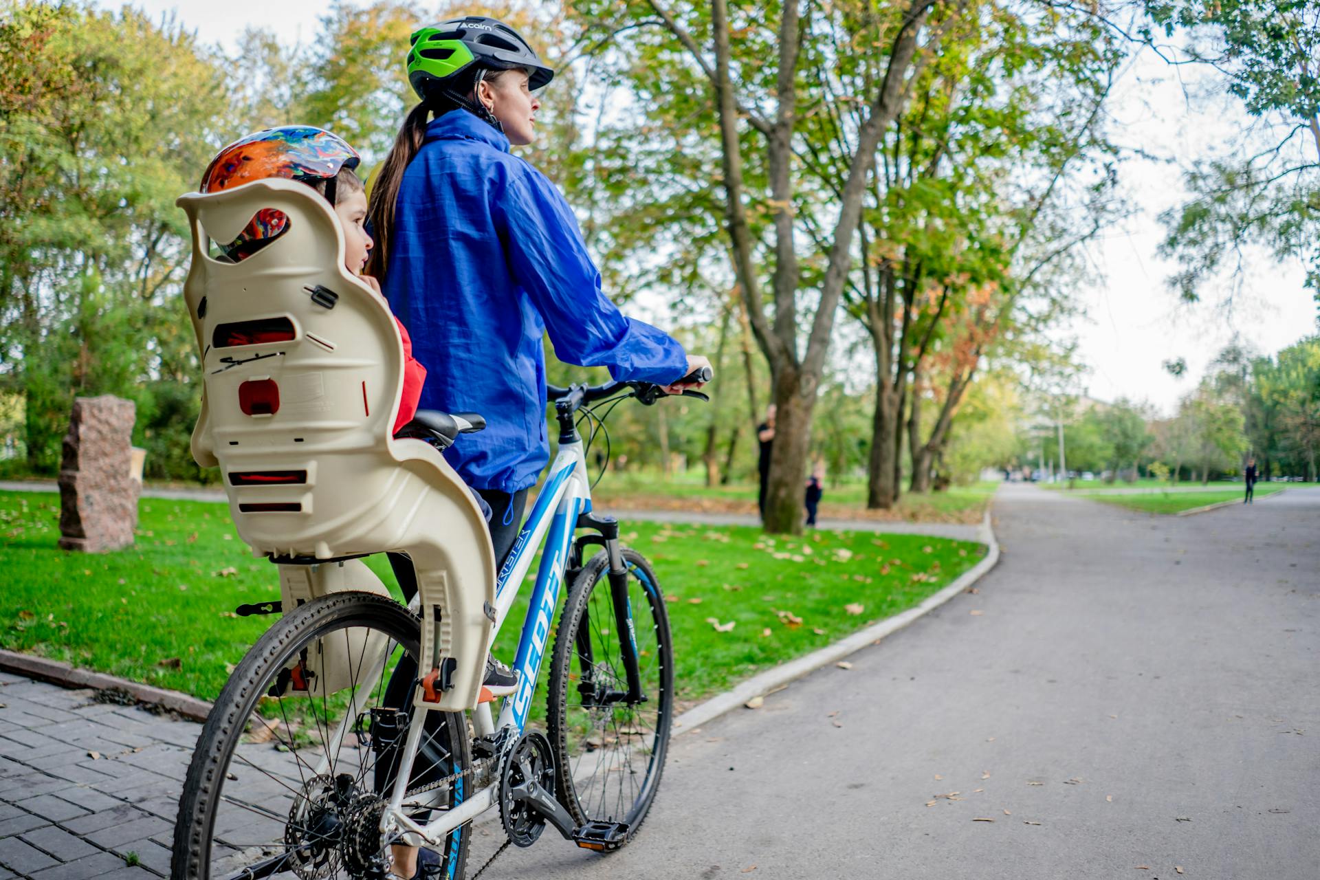 A woman rides a bike with a child seat outdoors in a vibrant park.