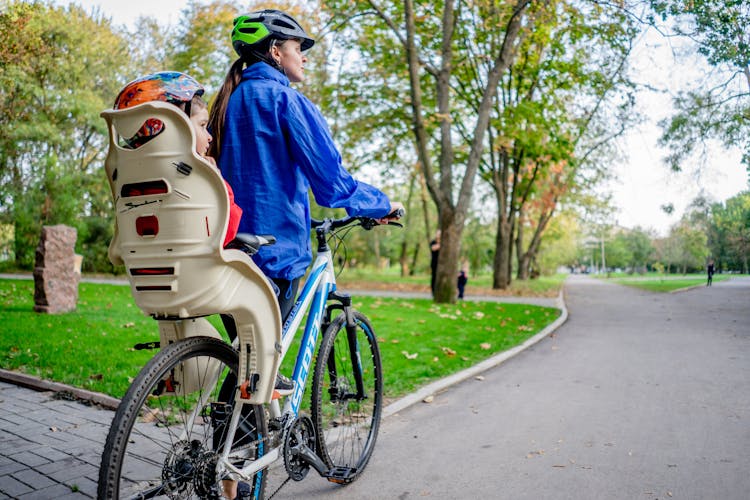 Woman And Child In Helmets Riding Bike In Park