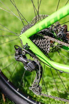 Detailed shot of a green bicycle gear and chain outdoors with a grassy background.