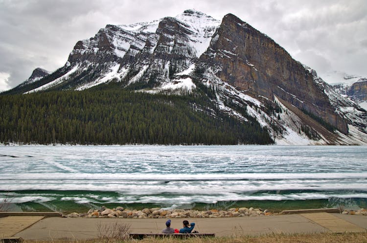 Two Persons Gazing At The Mountains Of Lake Louise In Alberta Canada