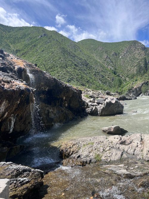 Free Scenic view of a rocky waterfall and river in a lush green mountain valley under a clear blue sky. Stock Photo
