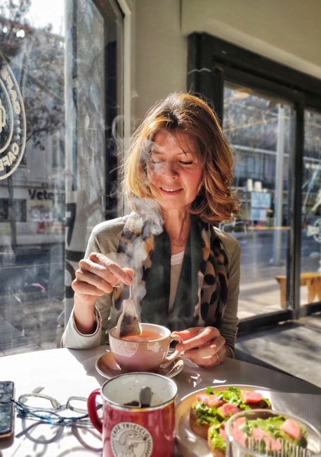 A woman adds a tea bag to her steaming cup of tea in a bright cafe.