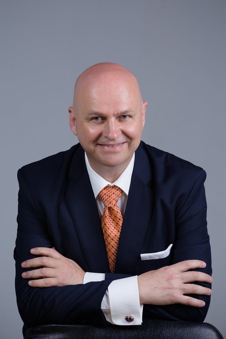 Man In Black Suit Jacket Leaning By The Chair While Smiling At The Camera