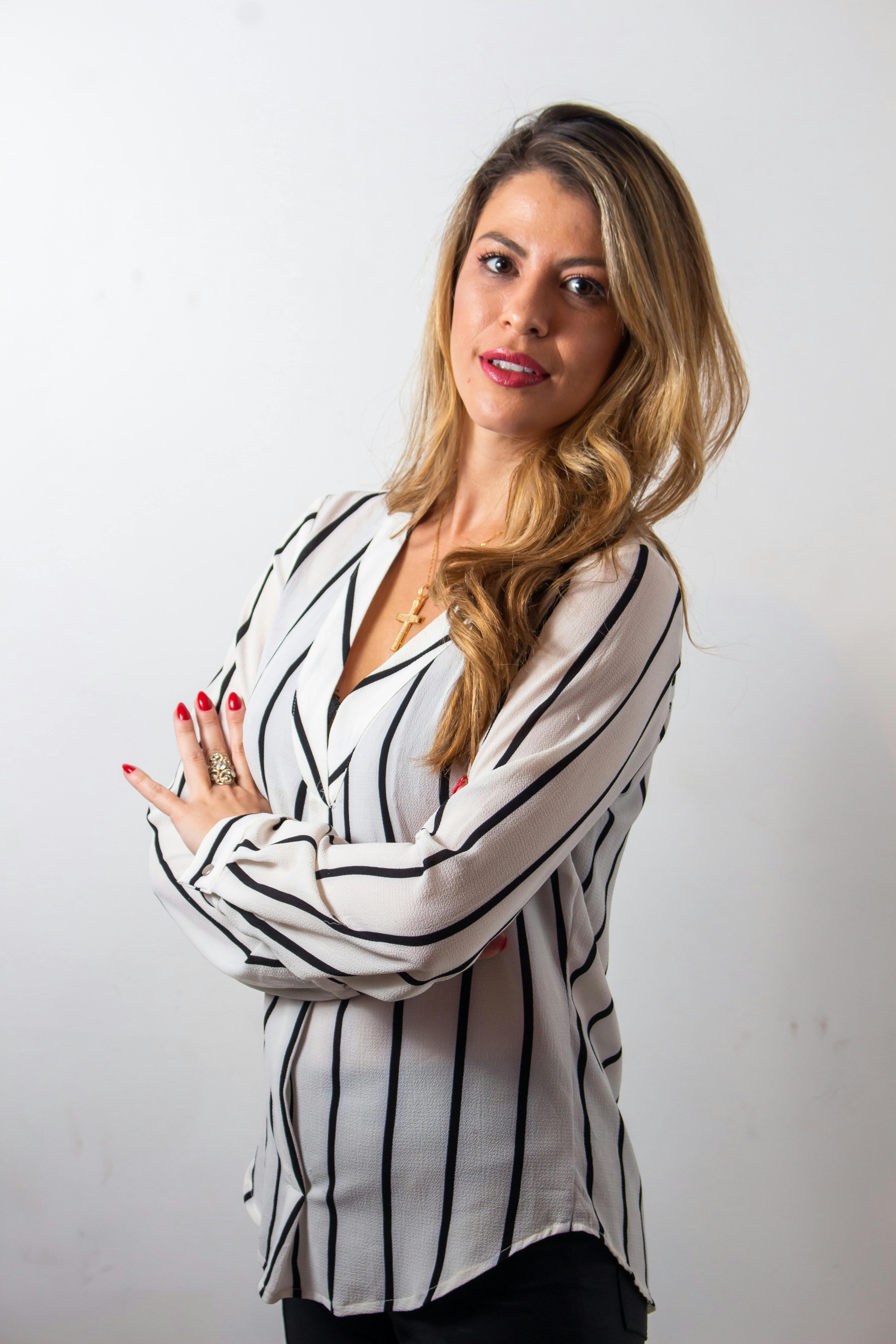 Portrait of a confident woman with blonde hair, arms crossed, in a studio setting.