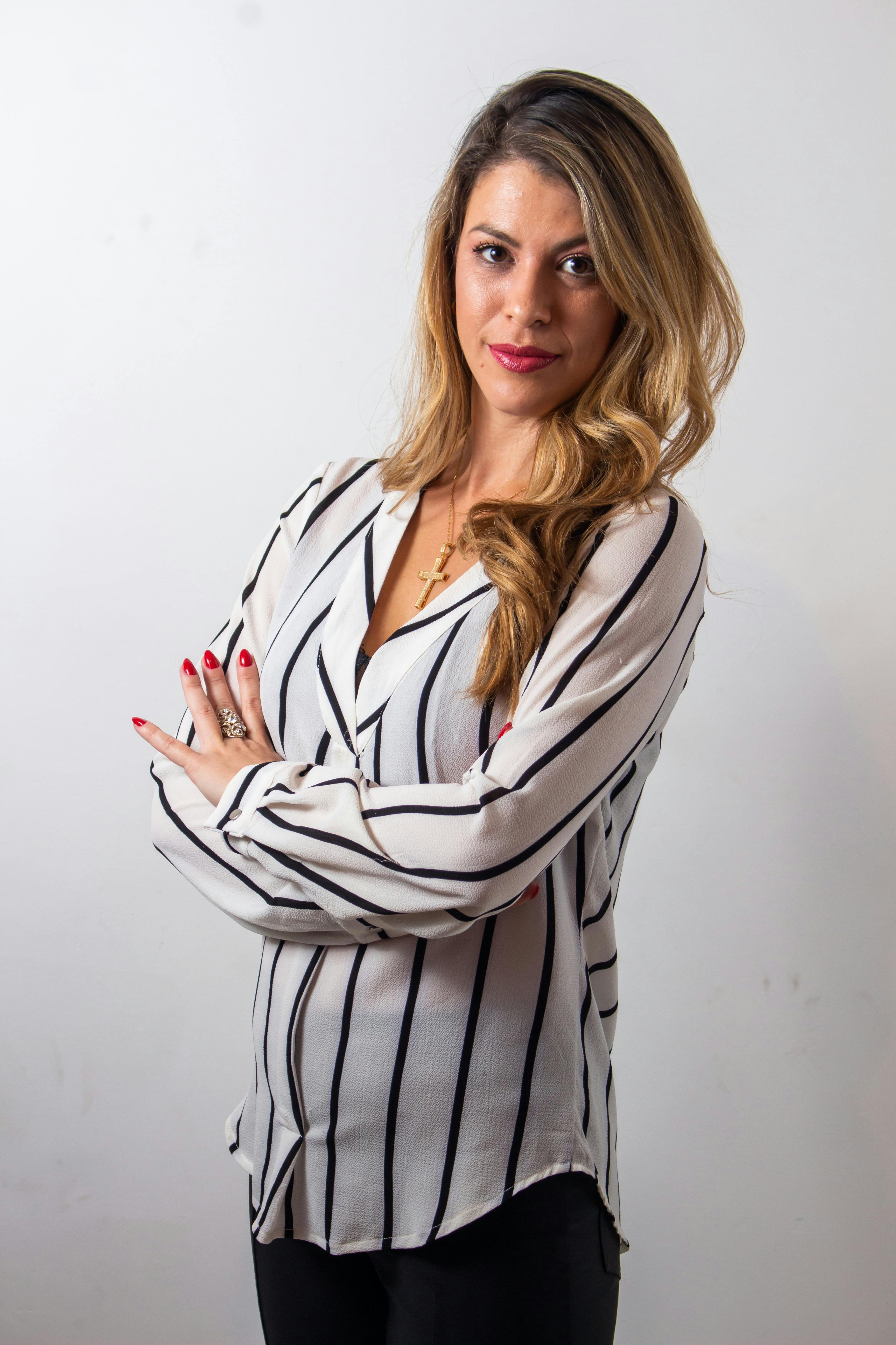 Portrait of a stylish woman with blonde hair in a striped blouse, posing confidently with crossed arms.