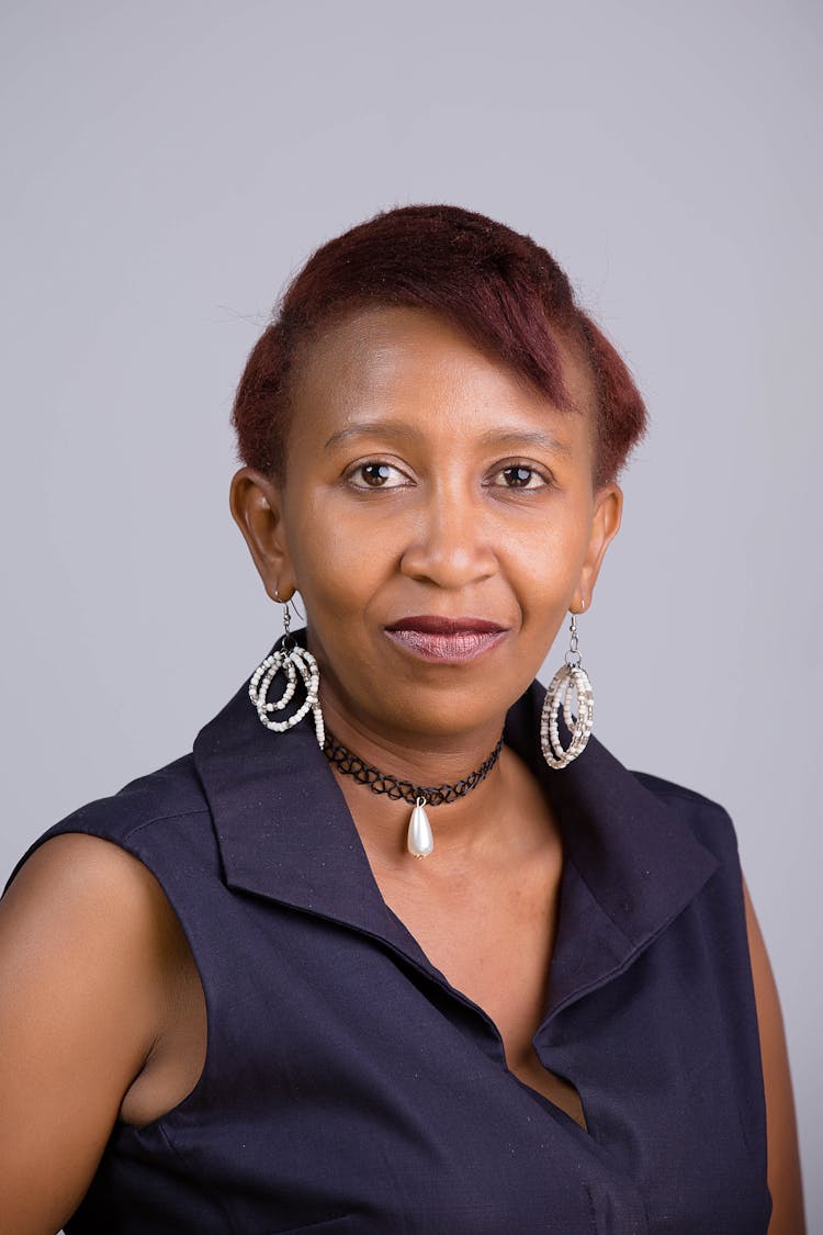 A Woman In Sleeveless Dress Wearing Earrings While Looking At The Camera