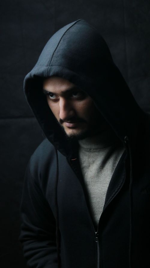 Free Dramatic portrait of a man wearing a dark hoodie against a dim backdrop, creating a mysterious atmosphere. Stock Photo