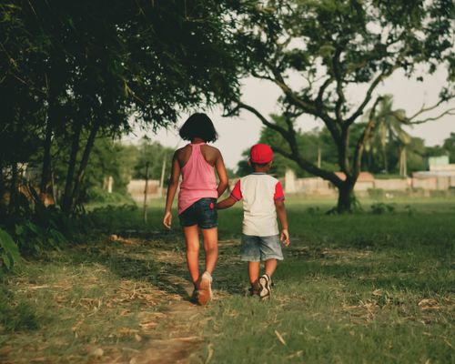 Free Young siblings walk hand in hand down a grassy path in a lush forest setting, capturing the essence of family bonding. Stock Photo