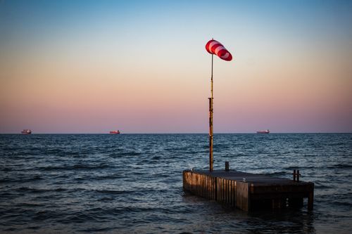 Free A serene view of the ocean with ships on the horizon and a windsock during twilight. Stock Photo