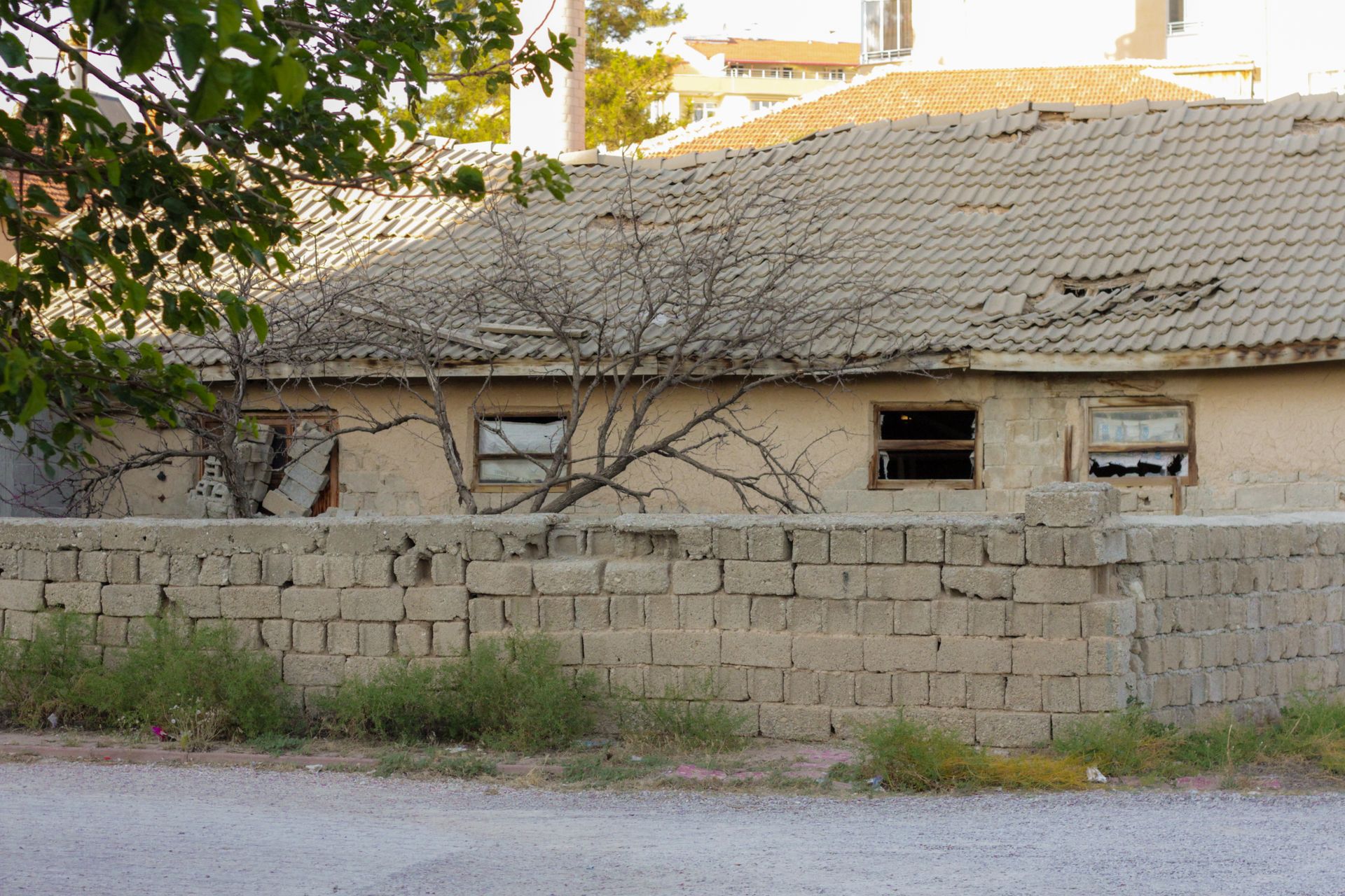 An old, abandoned house with broken windows and a stone wall in front.