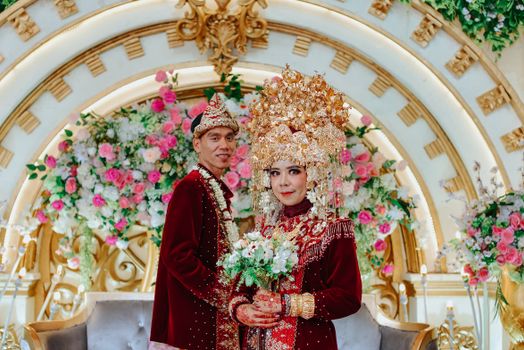 Asian couple in traditional wedding attire with floral backdrop. - Fotografer Sidoarjo