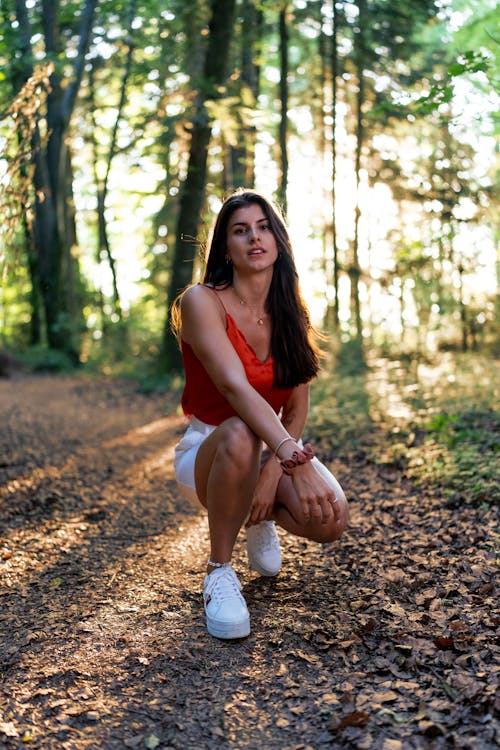 Free A Woman in Orange Tank Top and White Shorts Sitting on Ground With Dried Leaves Stock Photo