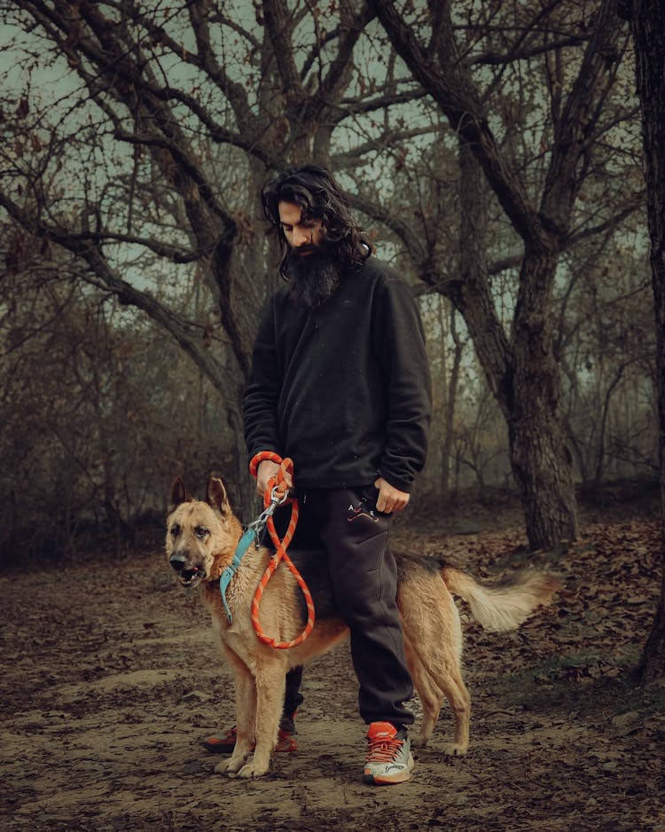 Man In Black Jacket And Pants Holding A Dog 