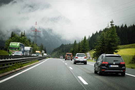 Cars and trucks on a foggy highway winding through lush Austrian Alps, creating a tranquil travel scene.
