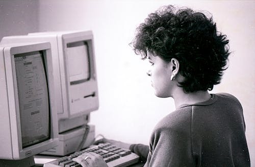 Black and White Photo of a Woman Using a Vintage Computer