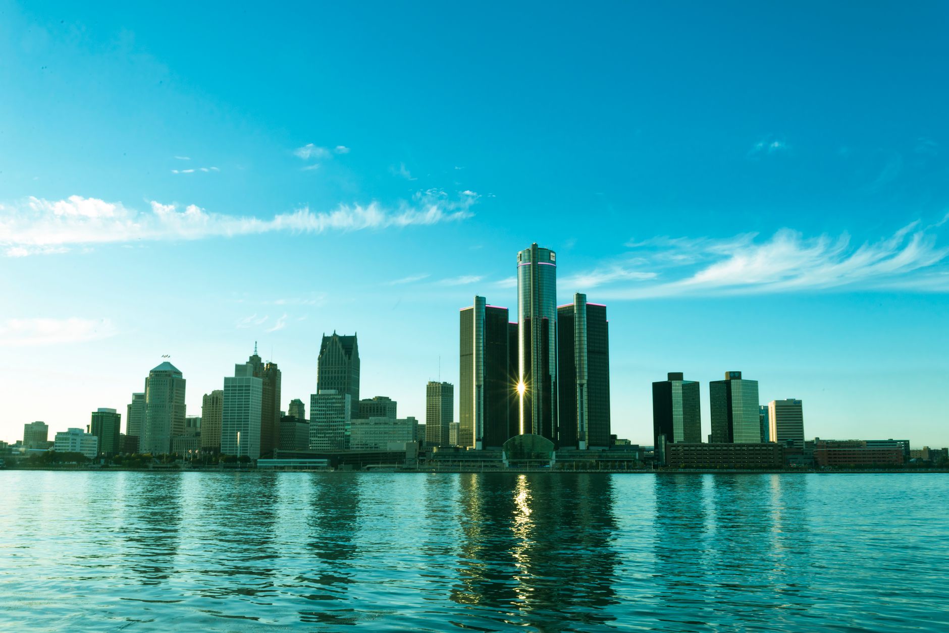 A beautiful view of the Detroit skyline reflecting on the river at sunrise, showcasing modern skyscrapers.