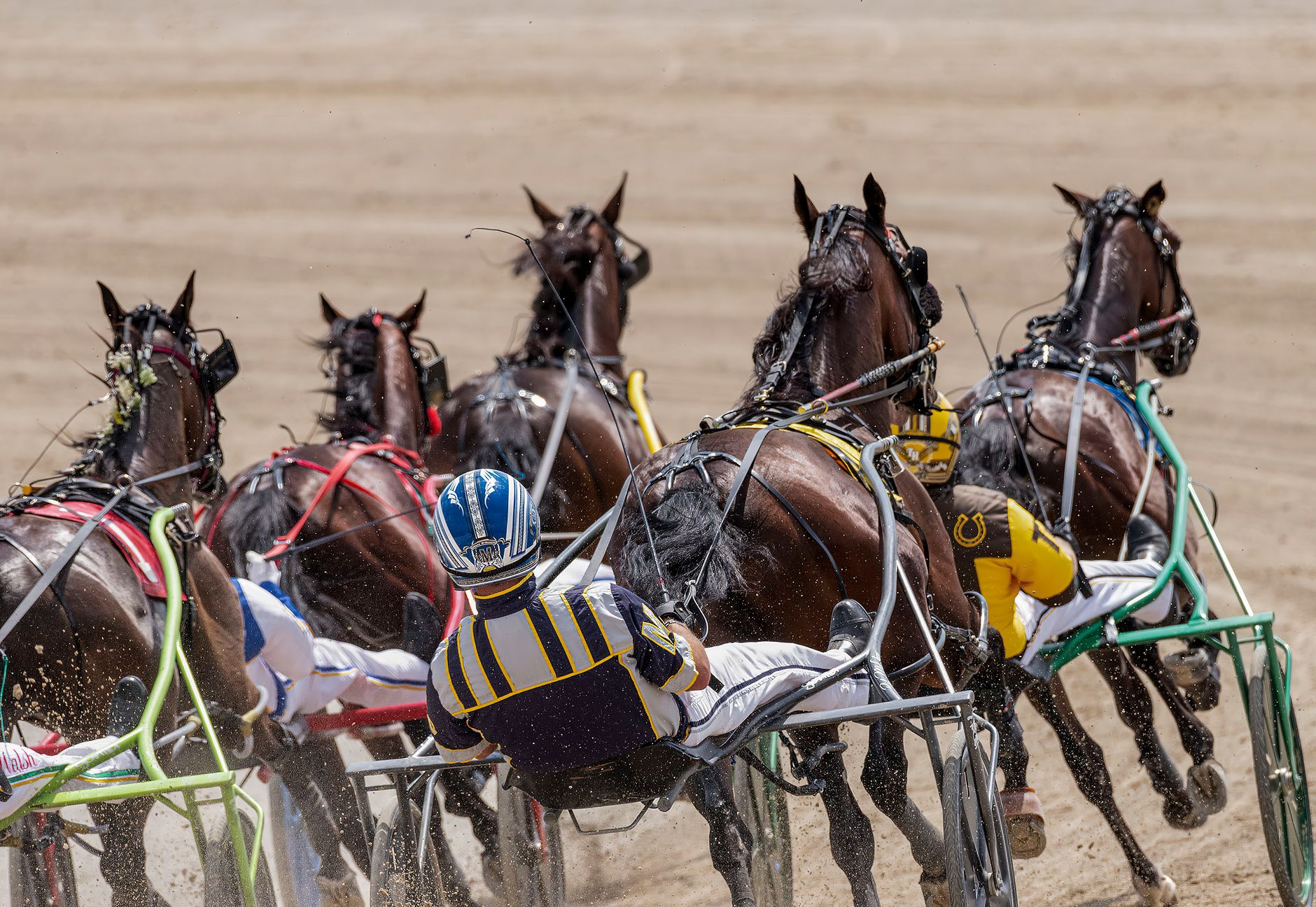 Dynamic harness racing scene with horses and drivers in action on a sandy track.