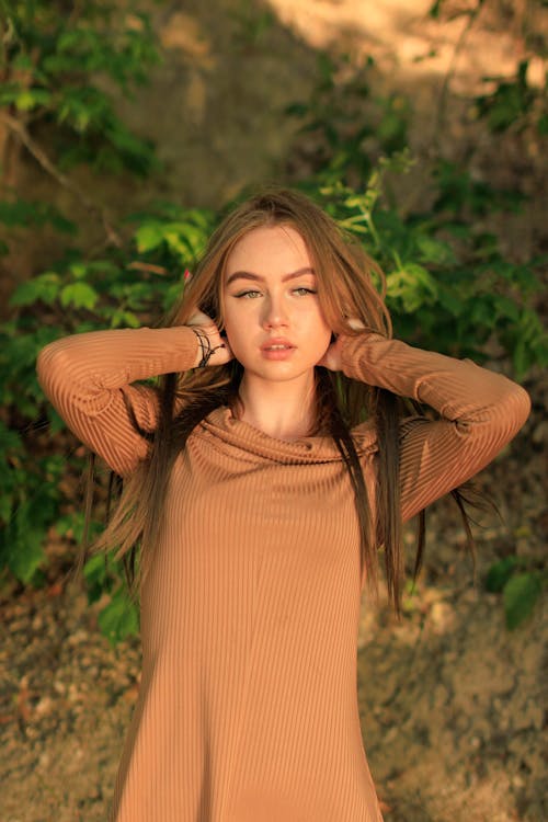 Beautiful Woman in Brown Long Sleeve Dress Fixing Her Hair 