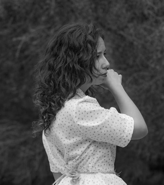 Black and white portrait of a woman in a polka dot blouse with wavy hair, posing outdoors.