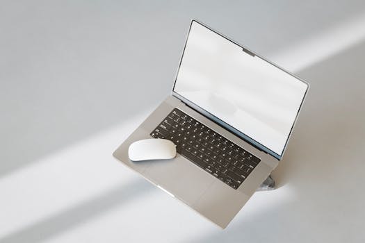 A modern laptop and mouse on a clean, white surface, with a minimalist aesthetic.