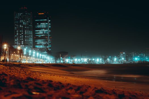 Illuminated skyscrapers and beach at night in Barcelona's vibrant urban landscape.