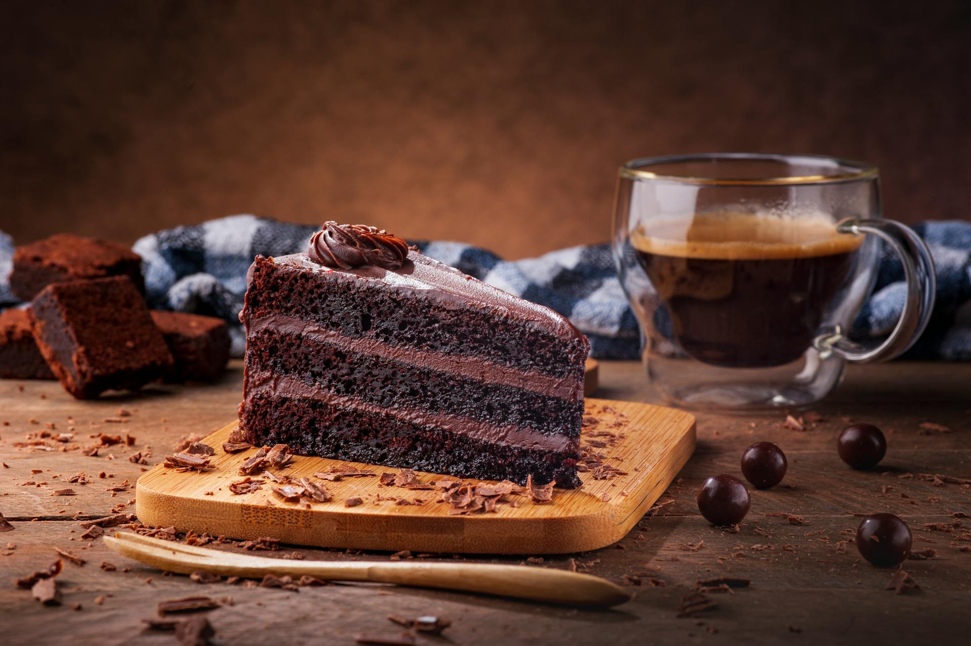 Rich chocolate cake slice on wooden board with espresso coffee for a sweet treat.