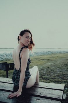 Woman in a swimsuit sitting on a wooden bench by the sea, gazing over her shoulder.