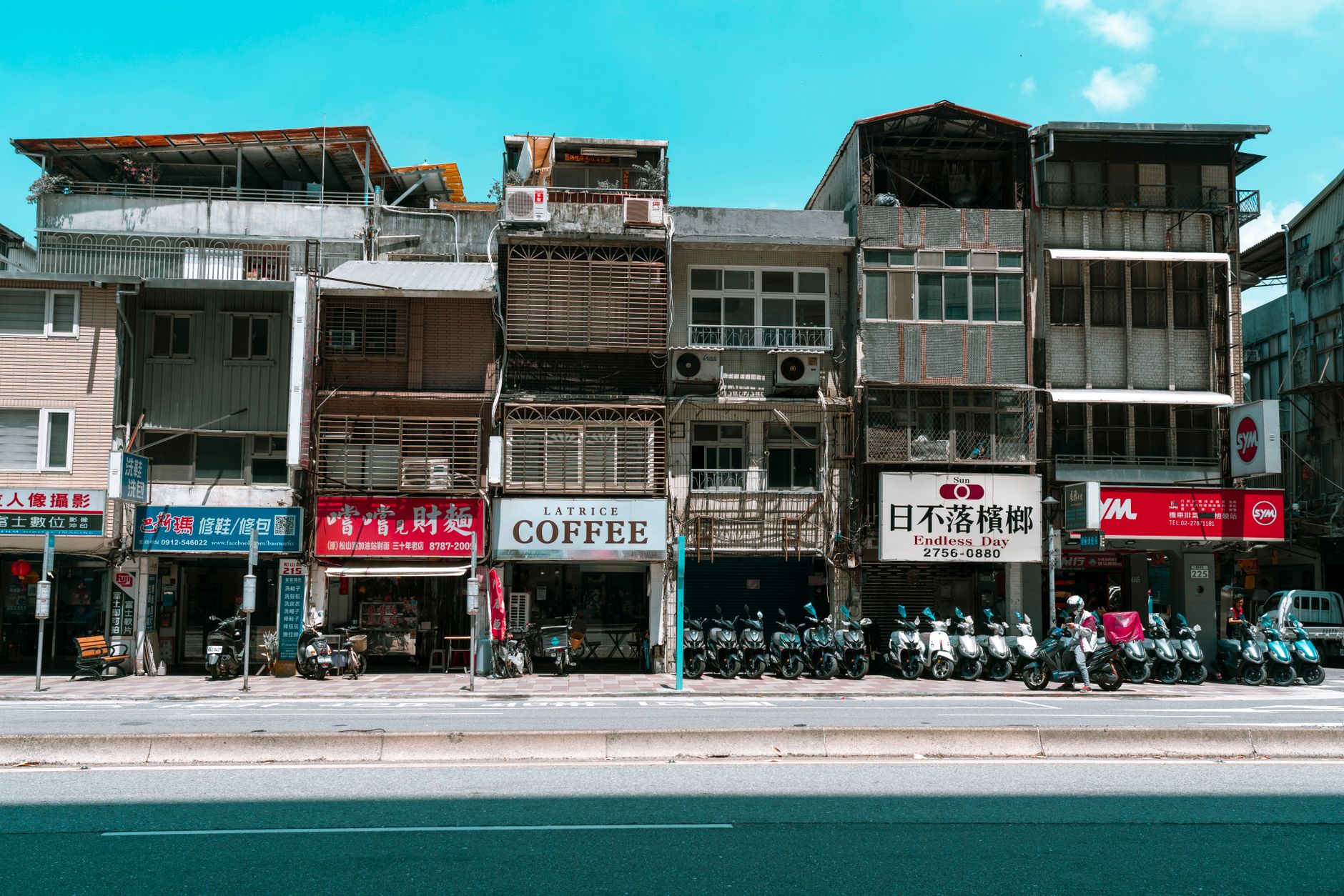 A vibrant street lined with shops and scooters in an Asian city, capturing local commerce and architecture.