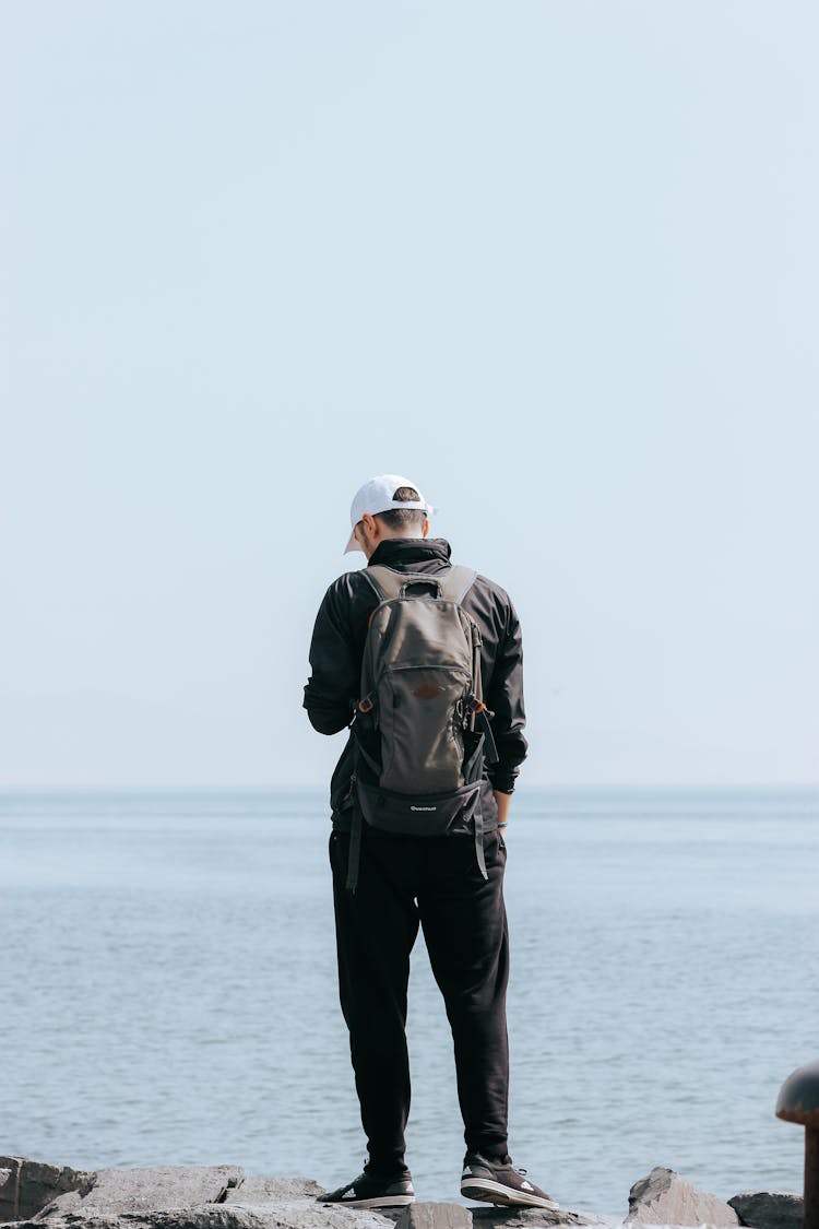 Back Of A Man With A Backpack Standing On A Shore