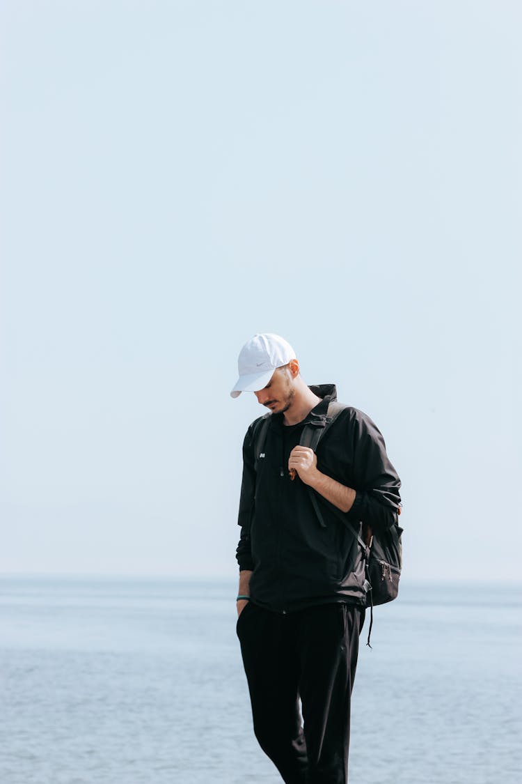 Man In Black Jacket And White Cap Wearing Backpack Looking Down