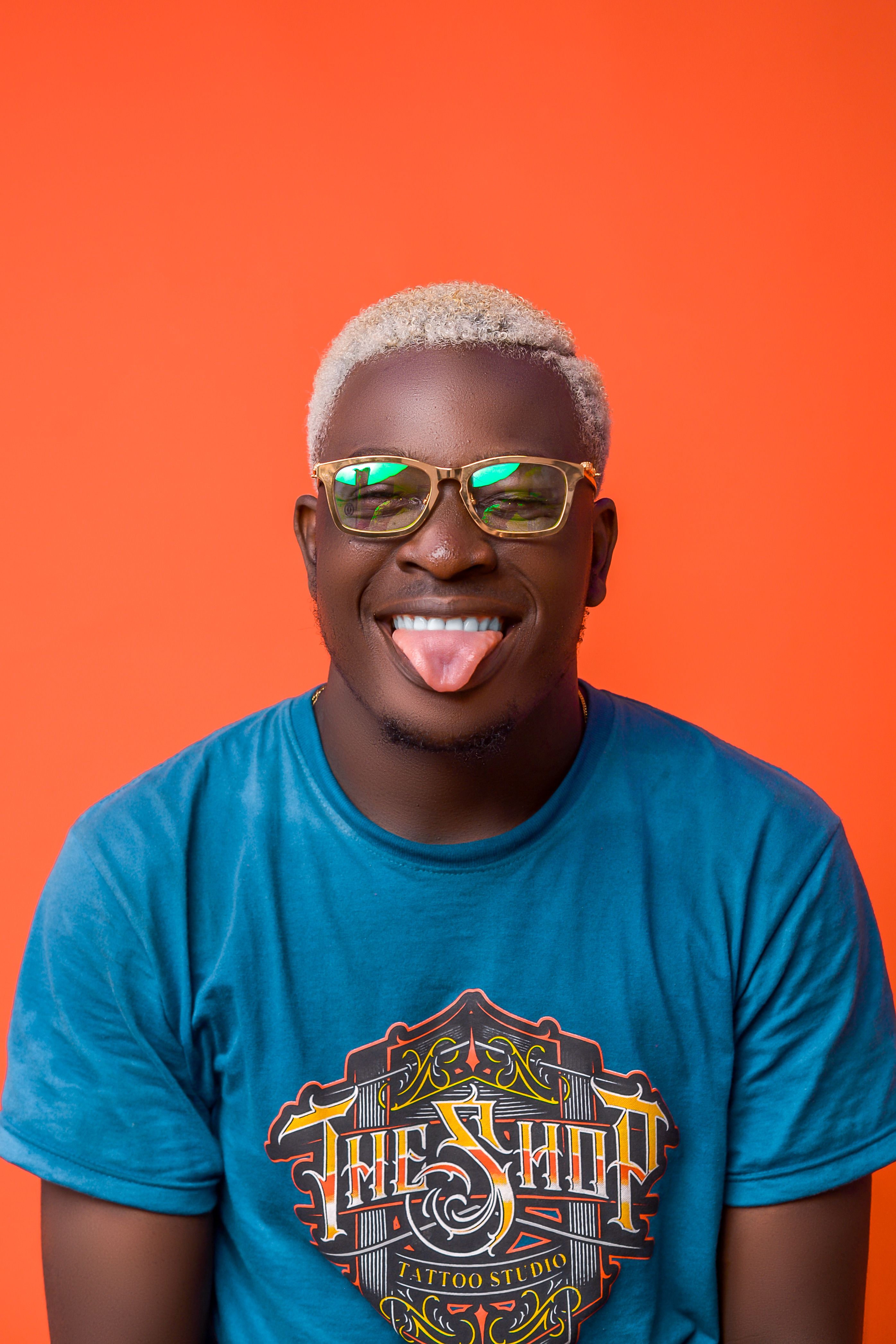 Portrait of a cheerful man with blonde hair and eyeglasses posing in a studio with an orange background.