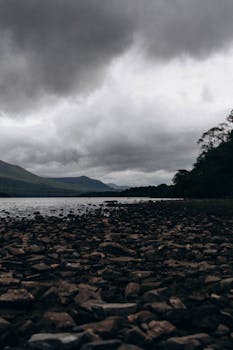 A moody view of a rocky shore with dark clouds gathering above, creating a dramatic scene.