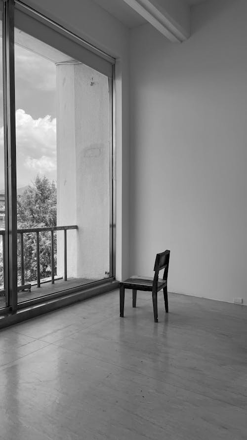 Grayscale Photo of Chair Near Glass Window