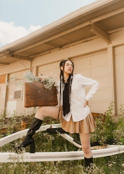 Stylish woman with long hair poses with a vintage suitcase in an urban outdoor setting. Fashion and travel concept.